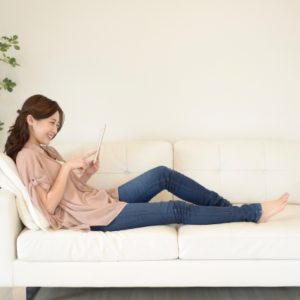 ソファでタブレットを見ながらくつろぐ女性